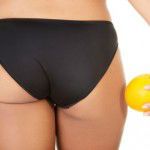 A girl holding an orange next to the buttocks