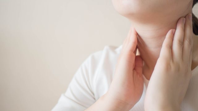 Female checking thyroid gland by herself. Close up of woman in white t- shirt touching neck. Thyroid disorder includes goiter, hyperthyroid, hypothyroid, tumor or cancer. Health care. Copy space.
