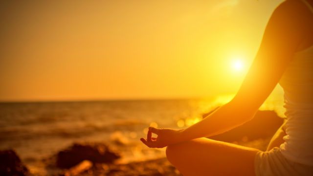 hand of woman meditating in a yoga pose on beach at sunset