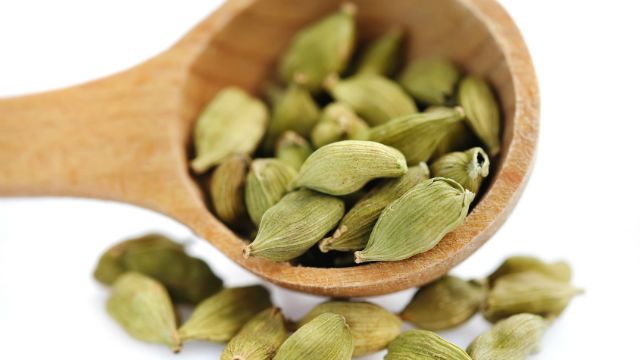 Cardamom seeds in the wooden spoon on white background