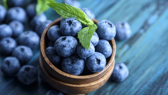 Bowl of fresh blueberries on blue rustic wooden table closeup.