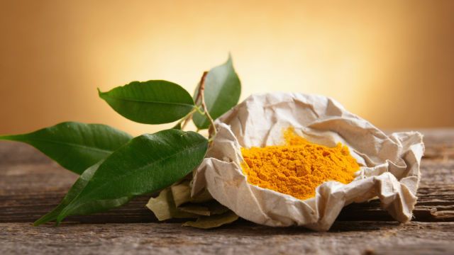 Tumeric powwder spice on wooden board with fresh leaves