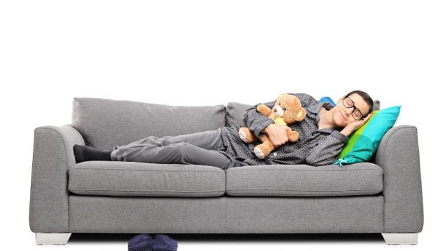 Young man in pajamas sleeping on couch with teddy bear