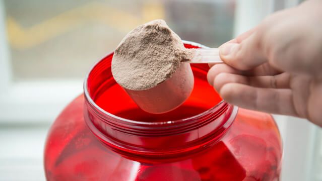 Man taking protein from container by the scoop.