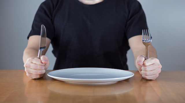 Man sitting at a table waiting for food, holding fork and knife