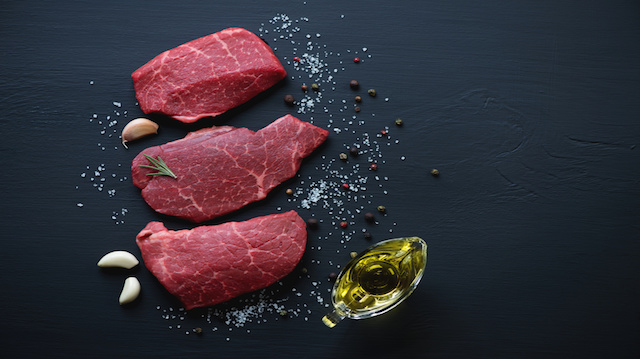 Raw marbled meat steaks with seasonings, black wooden surface