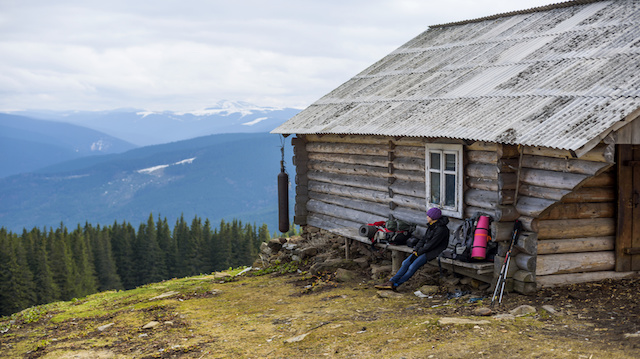hiker sitting near the wooden cabine in mountains