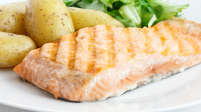 Grilled fillet of salmon on plate with green salad and potatoes.