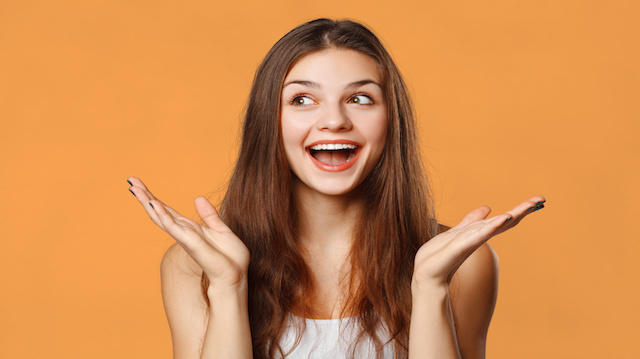 Surprised happy beautiful woman looking sideways in excitement. Isolated on orange background