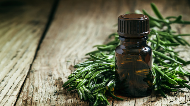 Rosemary essential oil in a small bottle and fresh rosemary on an old wooden background, selective focus
