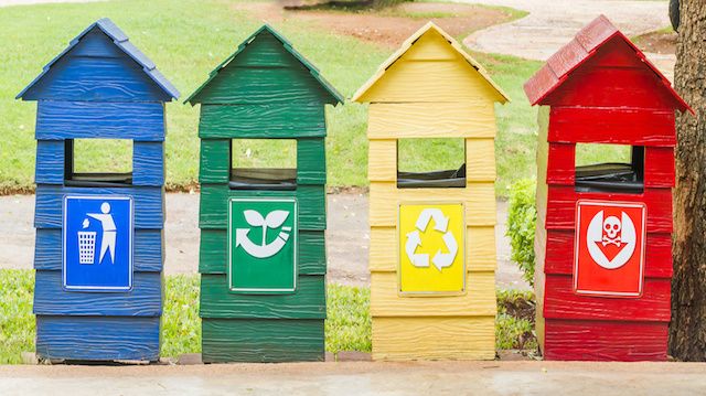 Blue, green, yellow and red bins on stand near footpath.
