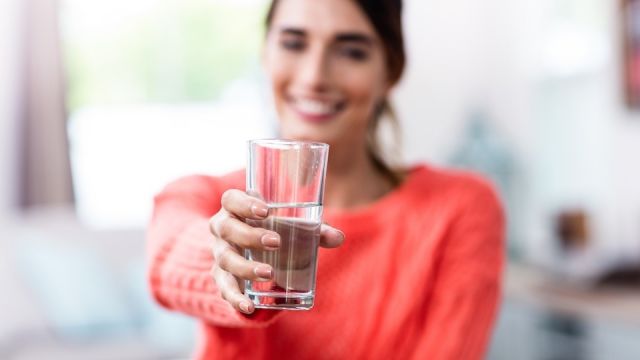 Young woman showing drinking glass with water